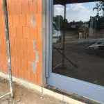 Fenster U-Wert einfach erklärt: Worauf Sie beim Kauf achten müssen, um Heizkosten zu sparen 4 Ziegelwand mit moderner Glasschiebetür in Baustelle; spiegelt ruhige Landschaft und deutet auf einen Neubau hin.