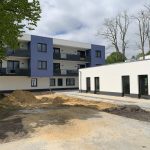 Erfolgreiche Fensterprojekte in Berlin & Brandenburg: Ein Blick hinter die Kulissen 4 Modernes Wohngebäude mit blauen Akzenten, umgeben von Bäumen, im Bau; klare Linien, helle Fassade, ruhige Umgebung.