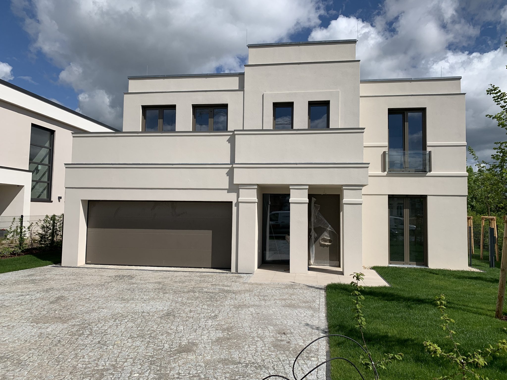 Modernes, zweistöckiges Einfamilienhaus mit Flachdach, großer Garage und gepflegtem Garten bei bewölktem Himmel.