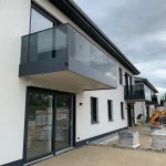 Was kosten neue Schüco- und PVC-Fenster inklusive Montage? 4 Modernes Doppelhaus mit Glasbalkonen und großen Fenstern; Baustelle im Vordergrund, grauer Himmel im Hintergrund.