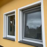 Fensterbänke Gewerbe Berlin 4 Zwei moderne, rechteckige Fenster in einer gelben Hausfassade mit weißen Rahmen und schwarzen Fensterbänken.