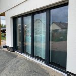 Schallschutzfenster von Sokobau 3 Moderne Schiebetüren aus Glas in einem Neubau, umgeben von Kiesfläche und Holzelementen im Außenbereich.